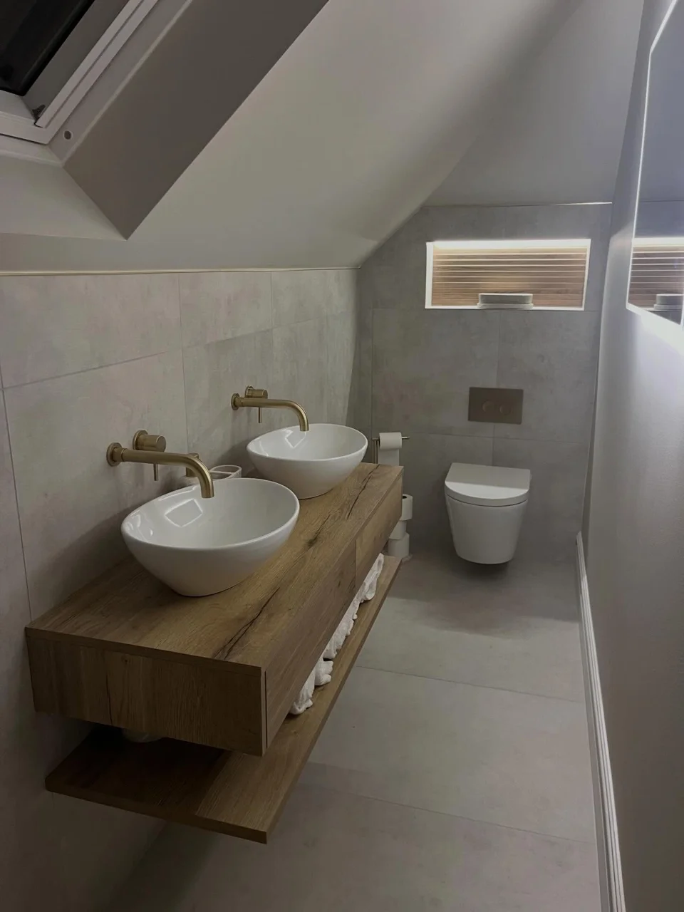 Two white vessel basins on a timber vanity beneath a sloped bathroom ceiling